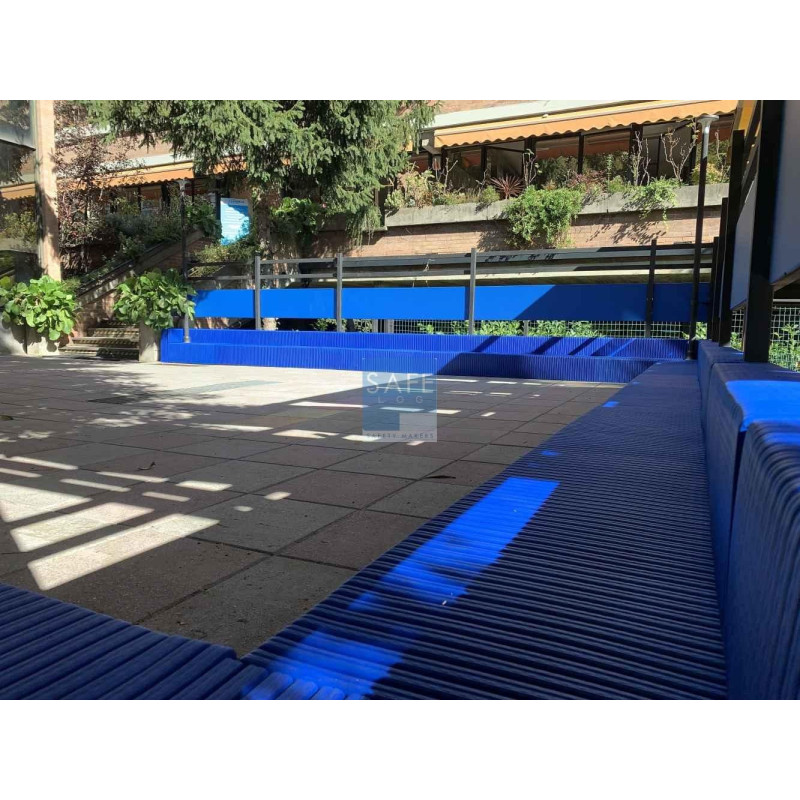 Bancs bleus modulaires en structure métallique entourant une aire pavée extérieure, avec garde-corps et ombres projetées, le tou