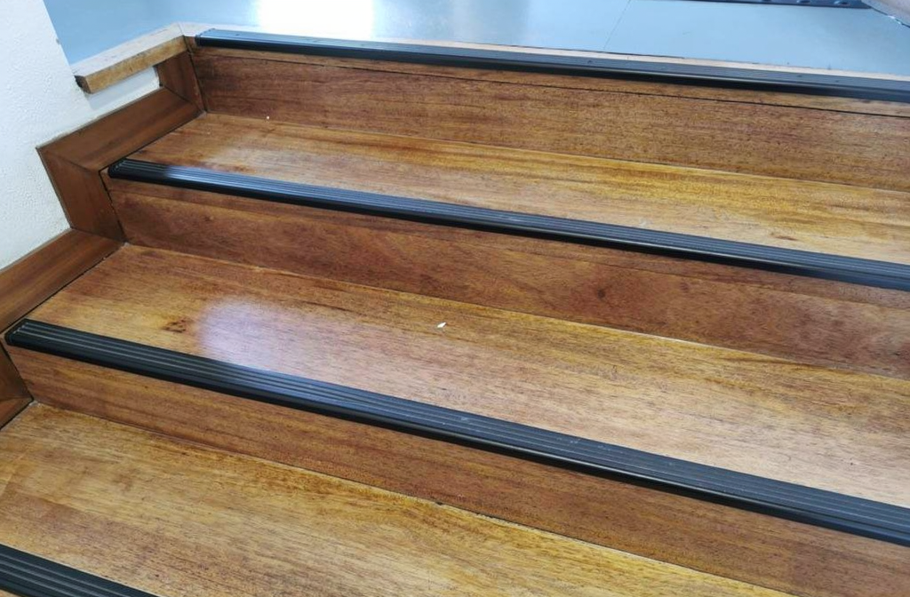 Nez de marche antidérapant installé sur les marches en bois d'un escalier commun d'immeuble collectif.