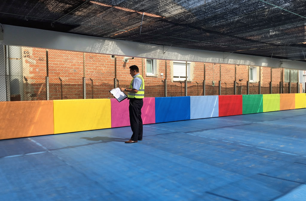 Inspecteur vérifiant la conformité des protections murales colorées dans une aire de jeux intérieure