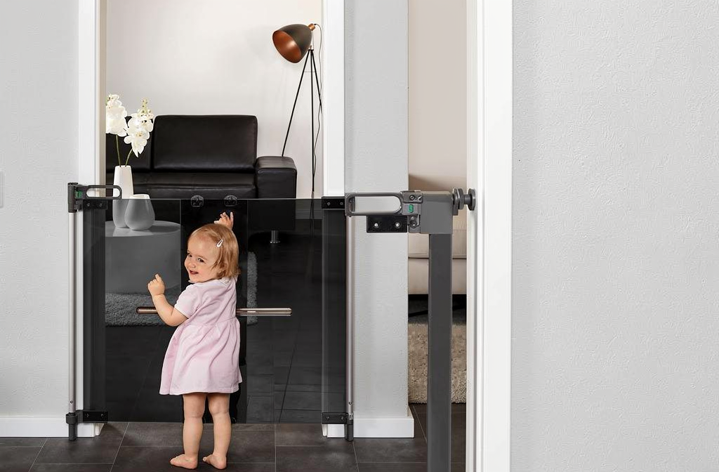 Barrière de sécurité enfant installée dans un couloir moderne avec un bébé souriant derrière la grille transparente.
