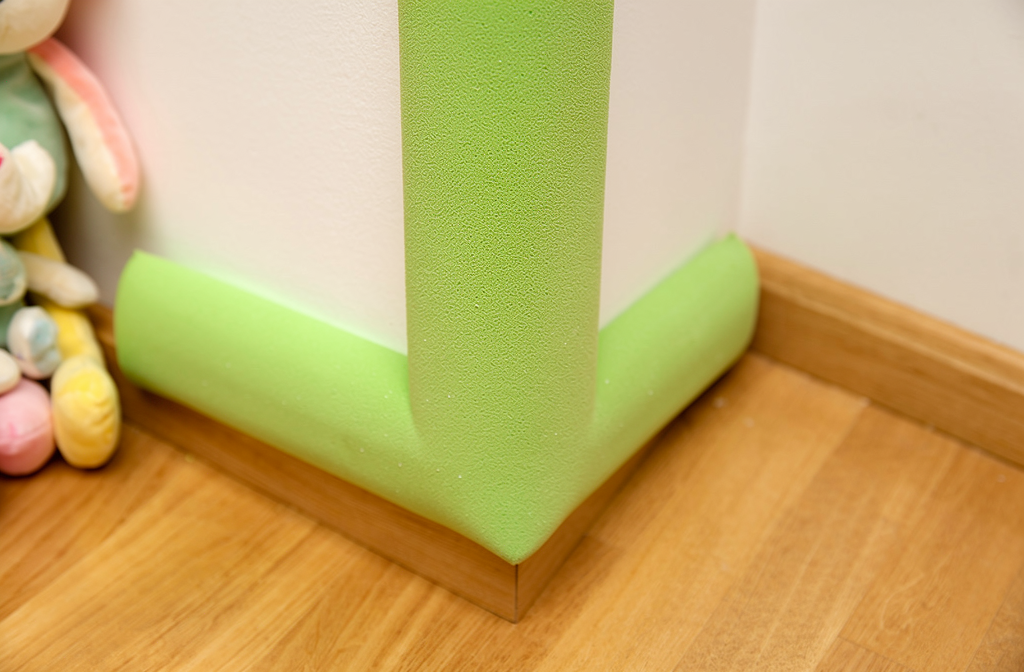 Protection en mousse verte installée sur un angle de colonne dans une crèche pour la sécurité des enfants.