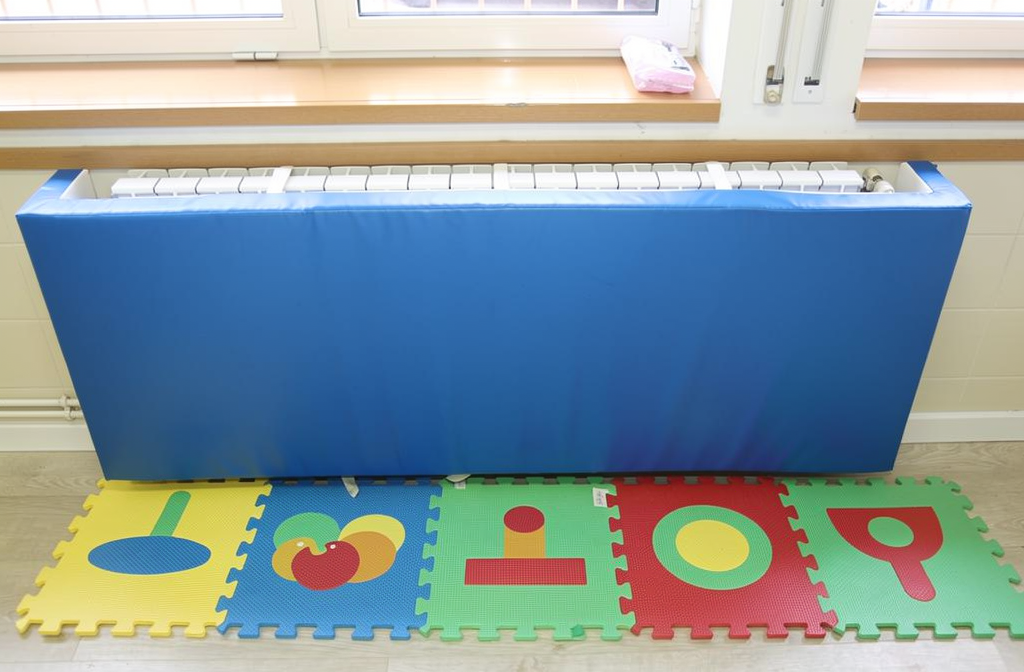Cache-radiateur bleu installé dans une chambre d'enfant lumineuse avec parquet et tapis de jeu.