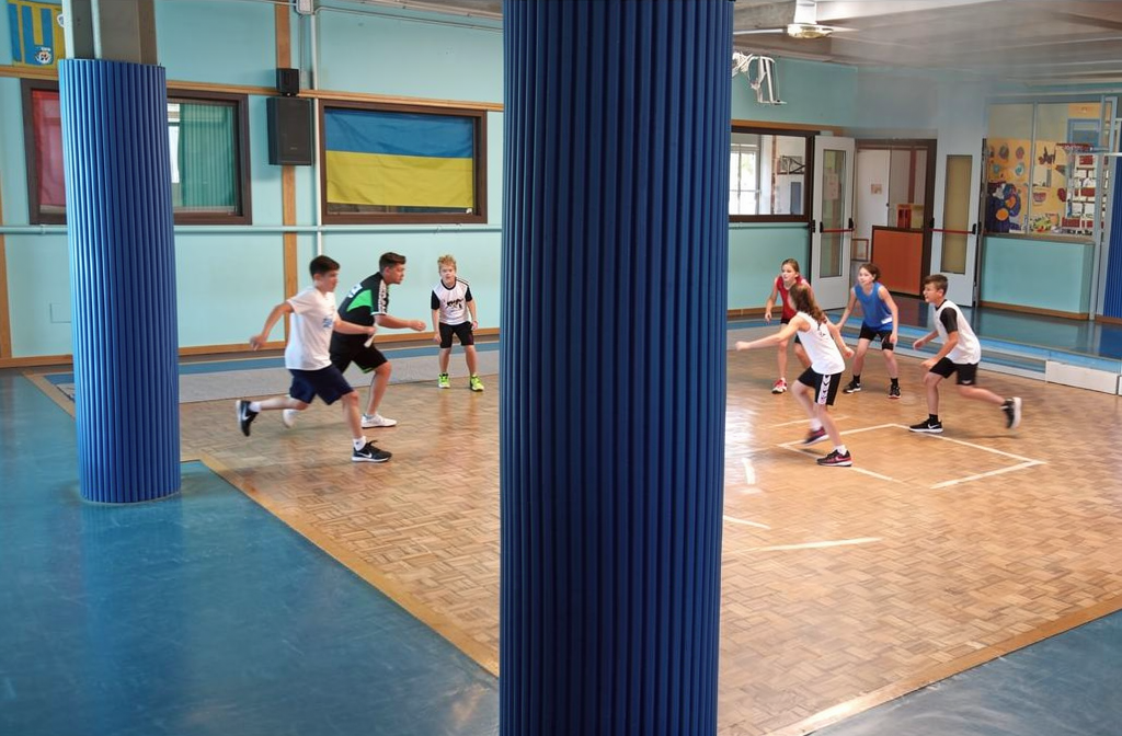 Protection de poteau ondulée bleue installée dans un gymnase scolaire pour la sécurité des élèves.