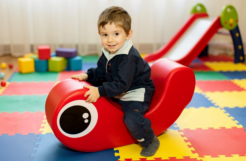 Siège ergonomique rouge pour enfant dans un espace d'activités motrices en crèche.