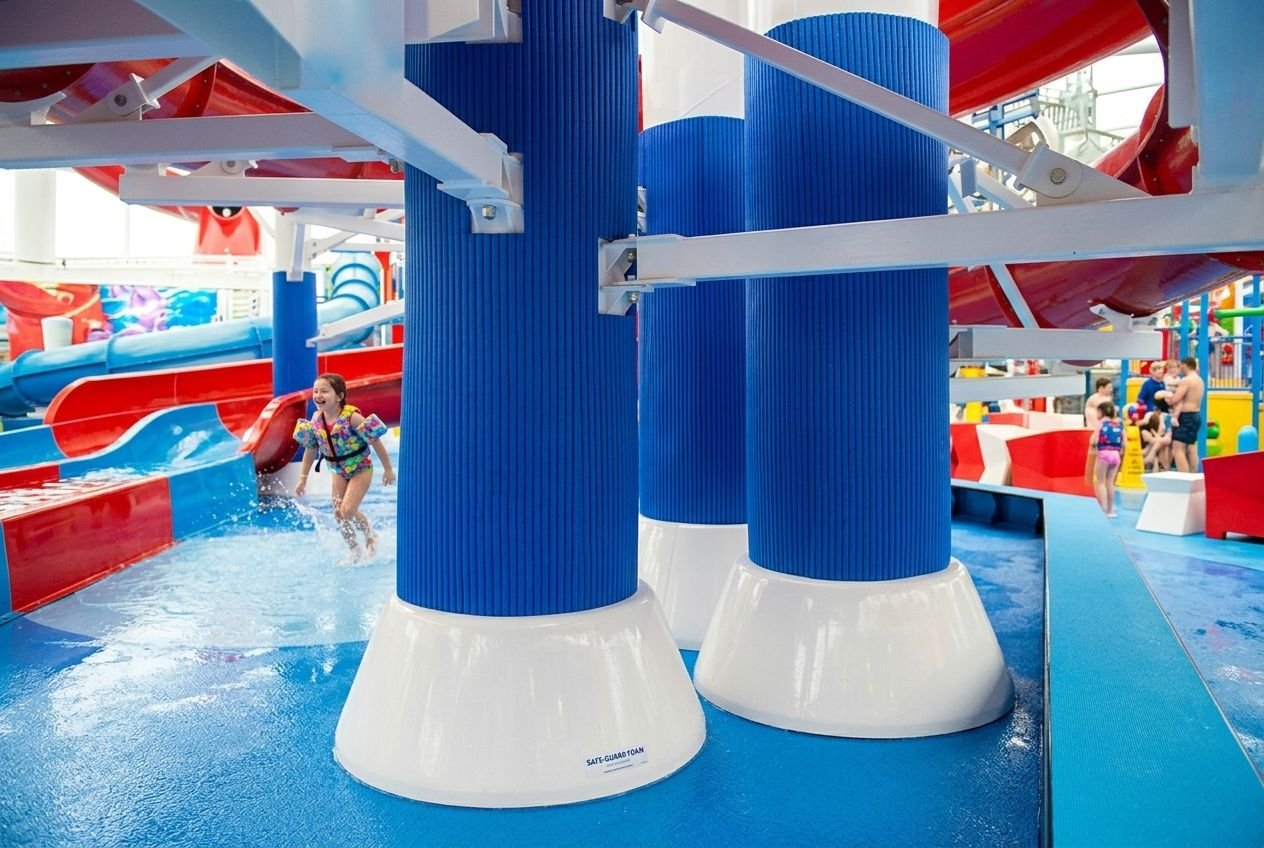 Protéctions en mousse pour poteau rond visibles dans une aire de jeux aquatiques, avec piliers bleus et bases blanches. protection mousse poteau rond en contexte commercial.