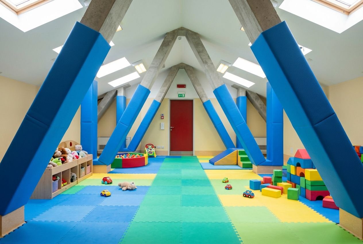 Salle de jeux intérieure colorée avec murs et colonnes bleues padding, sol moquetté multicolore et jouets. idée aménagement aire de jeux adaptée.