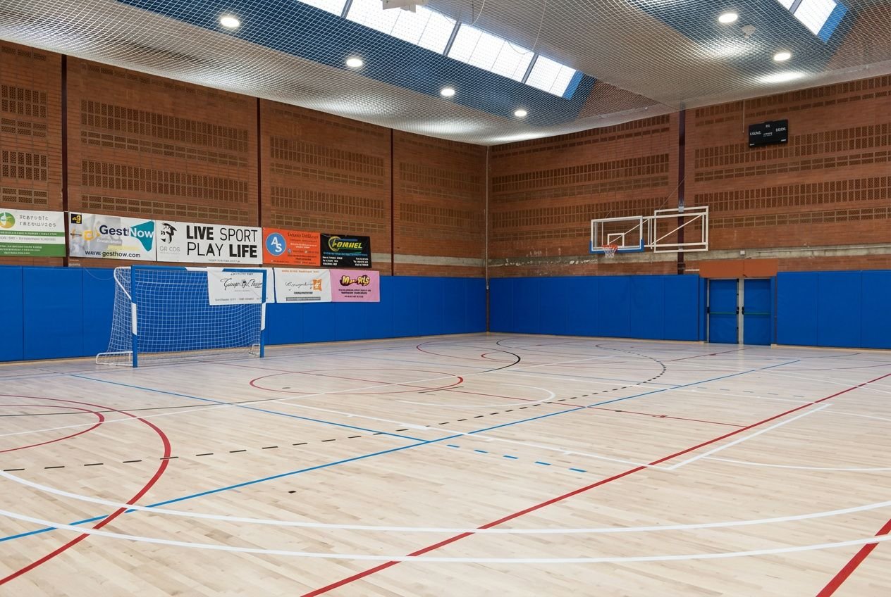 Salle sportive intérieure avec murs recouverts de protections bleues et panneau publicitaire, sol en bois et repères de jeu. Comment protéger les murs contre les chocs.